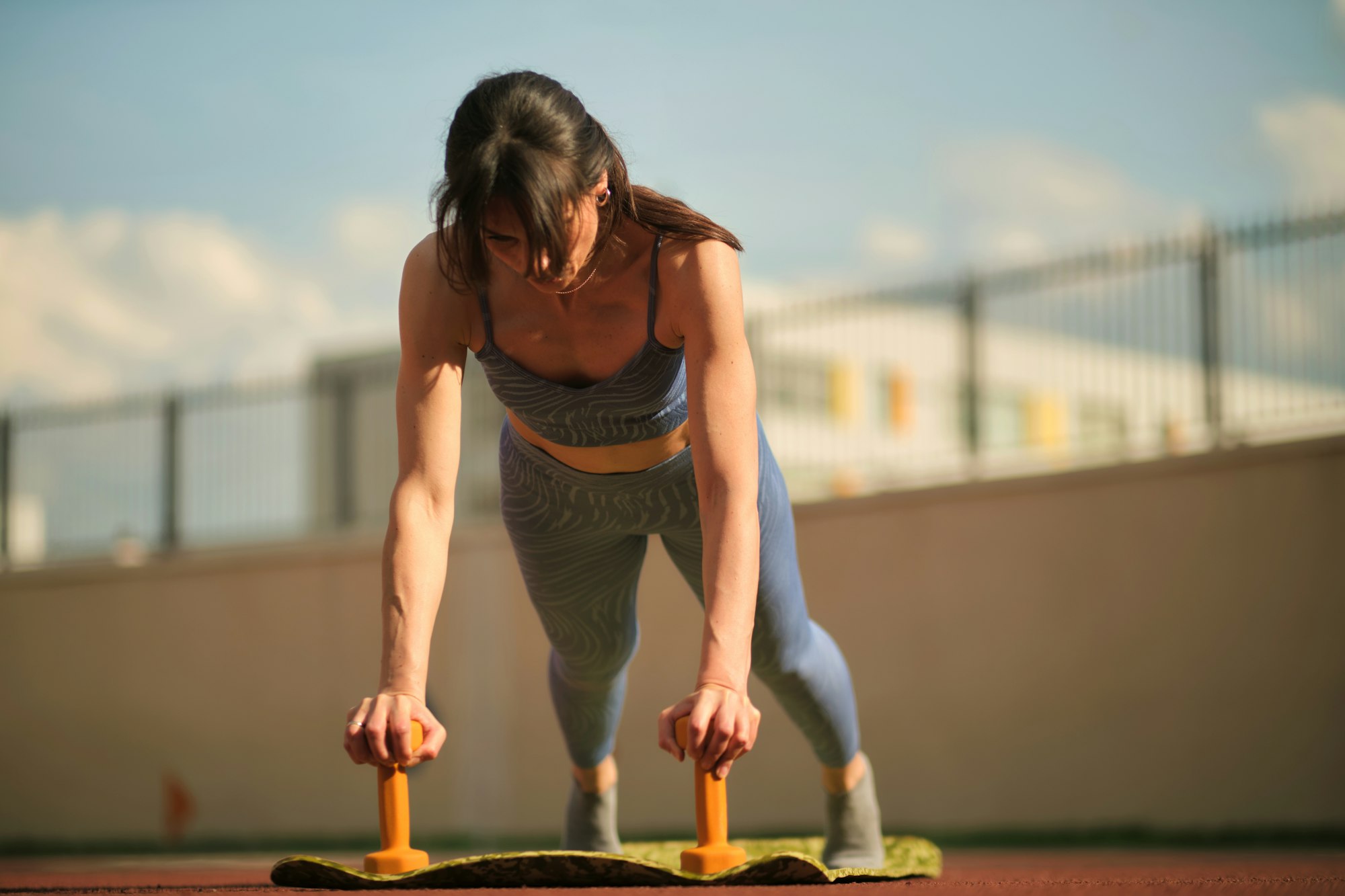 Exercising outdoors, the woman uses dumbbells to maintain a plank position, emphasizing upper body Exercising outdoors, the woman uses dumbbells to maintain a plank position, emphasizing upper body
